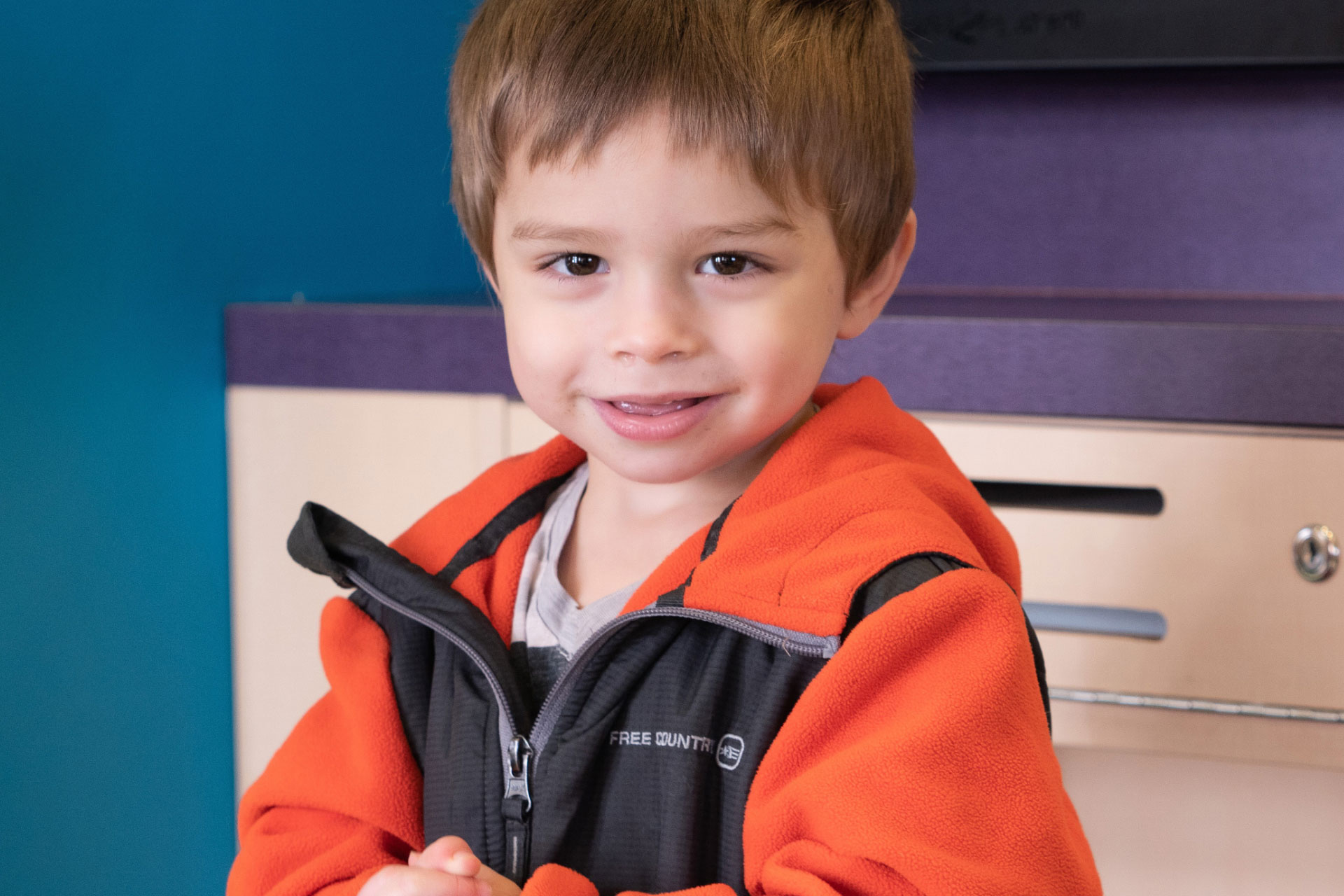 little boy wearing orange and black jacket smiling at camera
